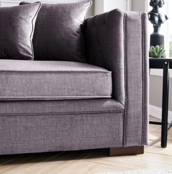 Grey fabric corner sofa with tufted arms and cushions beside window