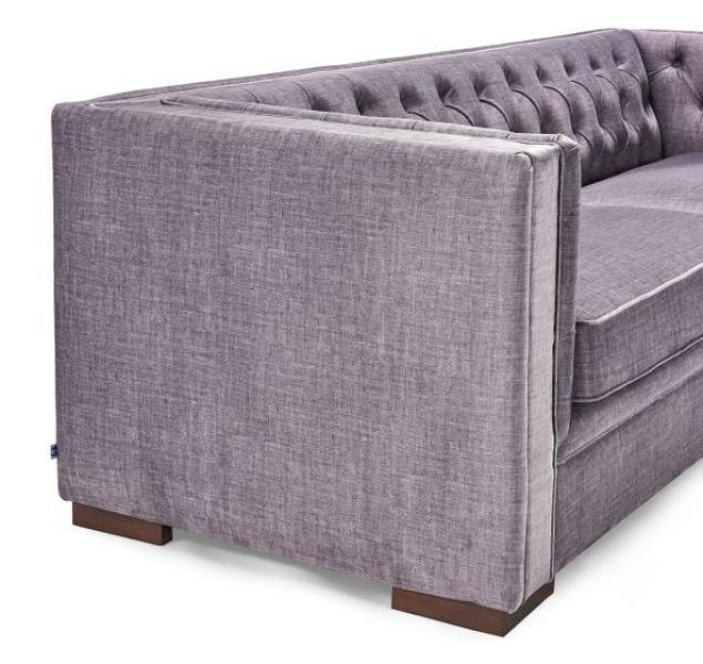 Grey fabric sofa with button-tufted back and modern wooden legs, side angle view