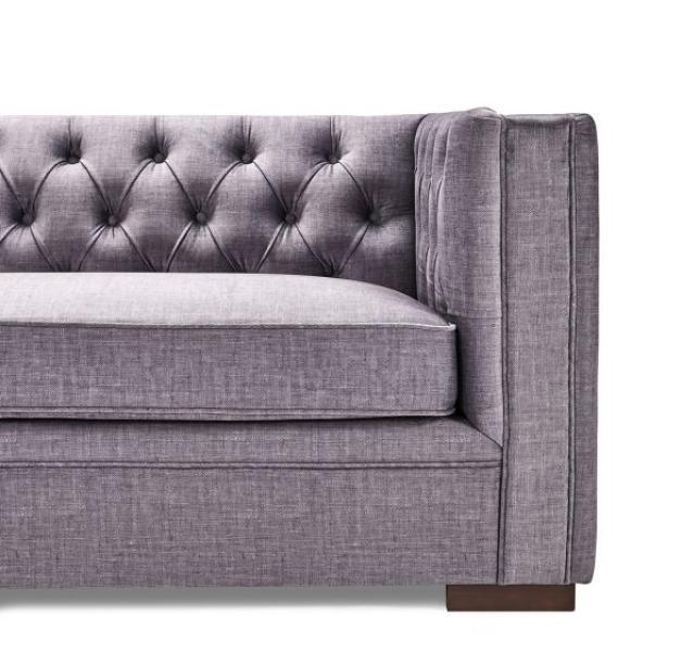Grey fabric sofa with tufted backrest and square armrest, partial side view