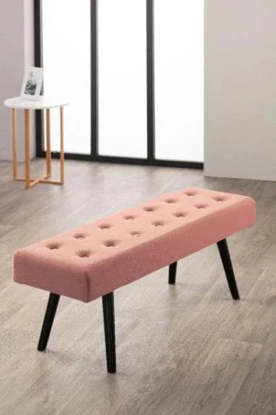 Pink upholstered bench with black angled legs on wood floor near window