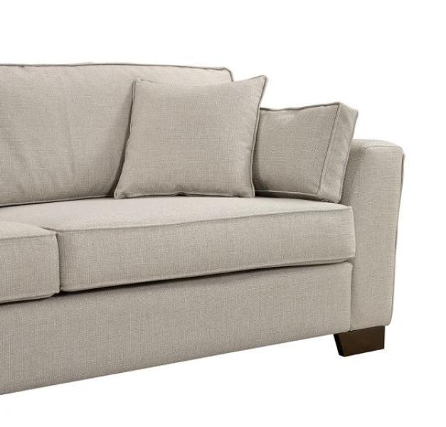 Beige fabric sofa with square armrest and matching scatter cushions, wooden legs visible