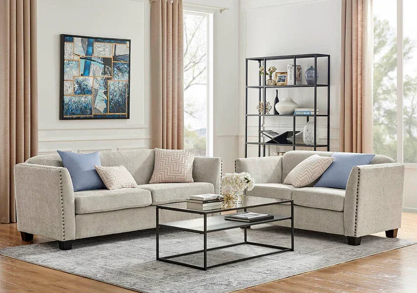 Light grey fabric sofas with studded arms, glass coffee table, and shelving in modern living room