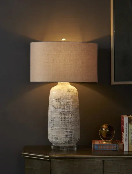 Ceramic table lamp with textured white base and beige fabric shade on sideboard