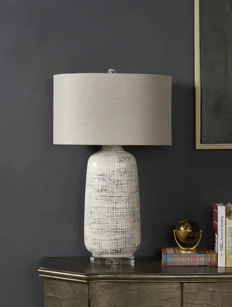 Ceramic table lamp with textured white base and beige fabric shade on sideboard