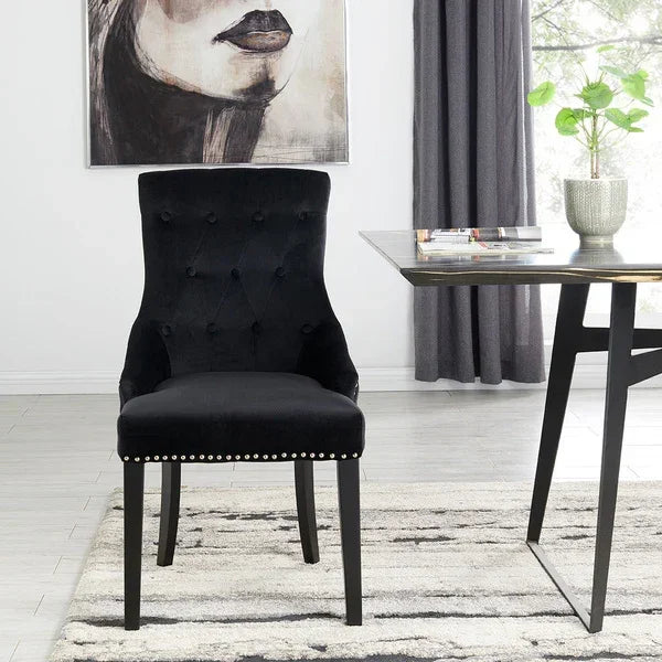 Black velvet dining chair with button-tufted backrest and silver stud trim in modern room