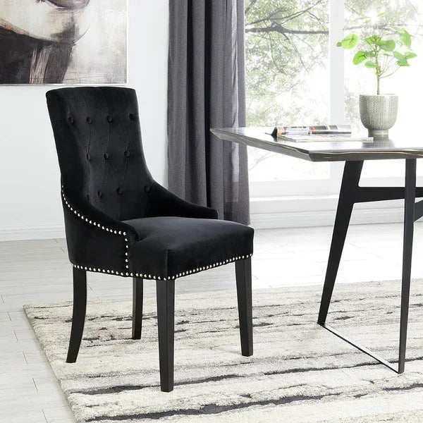 Black velvet dining chair with button tufted back and studded trim beside modern table