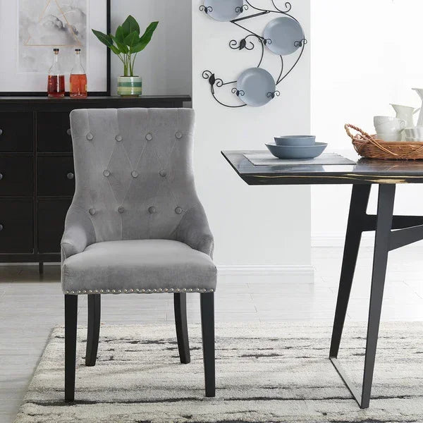 Grey velvet upholstered dining chair with button tufting and dark wood legs beside dining table