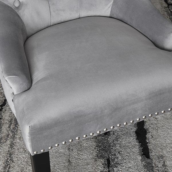 Grey velvet accent chair with silver stud detailing and black wooden legs on textured rug