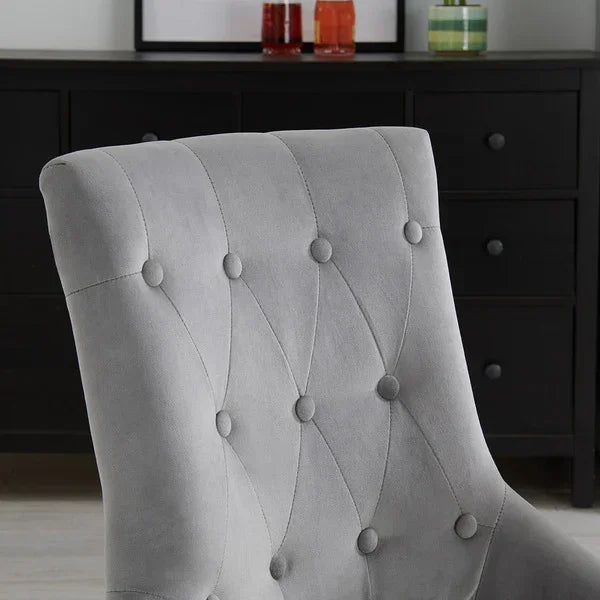 Light grey upholstered chair with button tufted backrest in front of black dresser