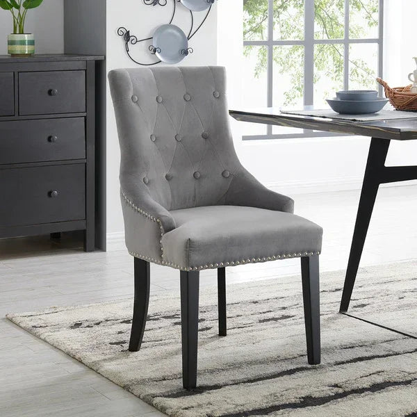 Grey velvet dining chair with button-tufted back and studded trim in modern dining room