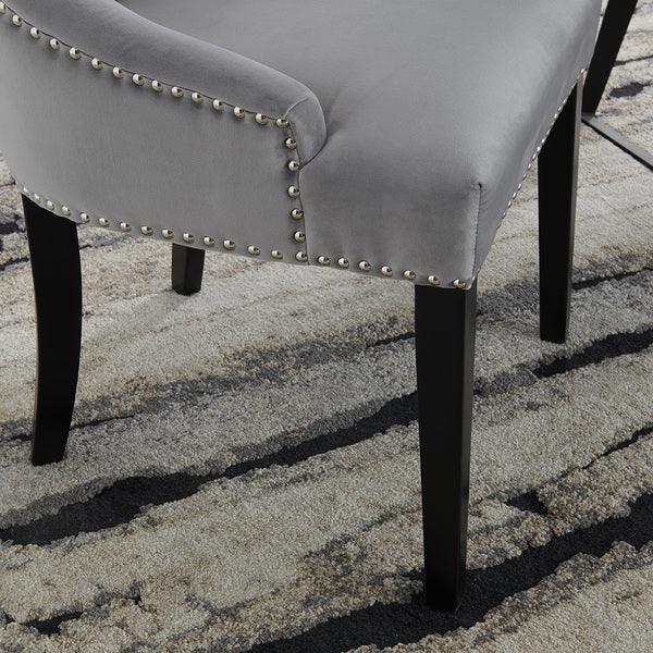Grey velvet dining chair with silver stud trim and black wooden legs on patterned rug