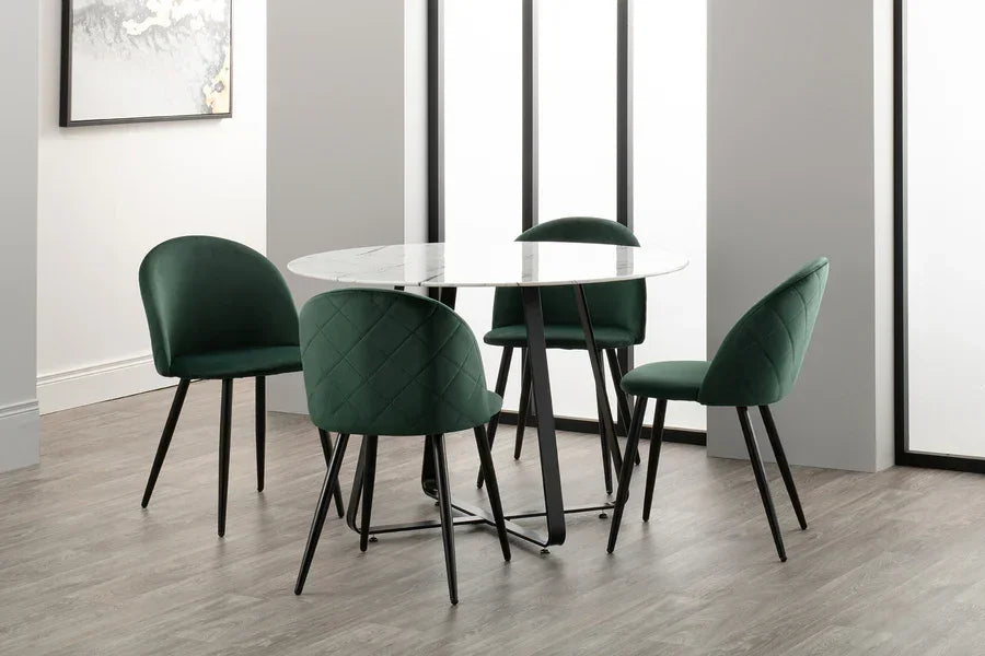 Round marble dining table with four green velvet chairs on wood flooring
