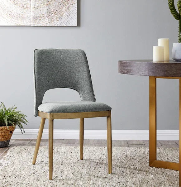 Grey upholstered dining chair with gold legs beside round wooden dining table