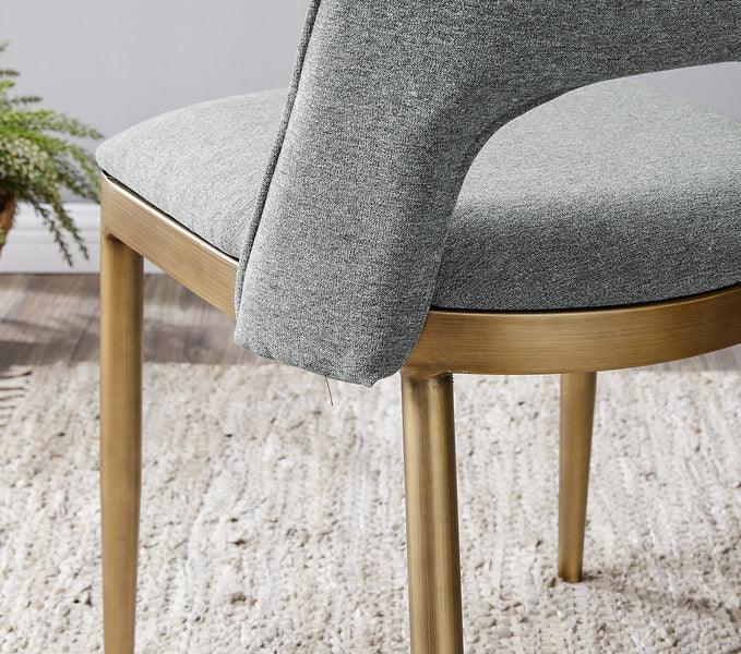 Grey fabric dining chair with curved back and gold legs on textured rug