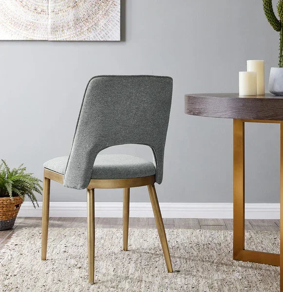 Grey upholstered dining chair with gold metal legs at round wooden dining table
