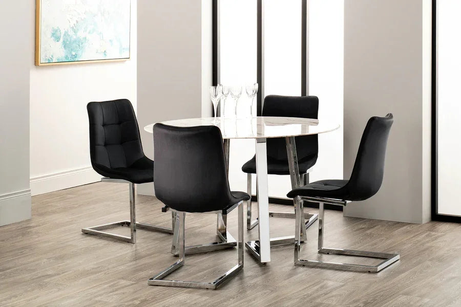 Round dining table with white marble top and four black velvet chairs on wooden floor