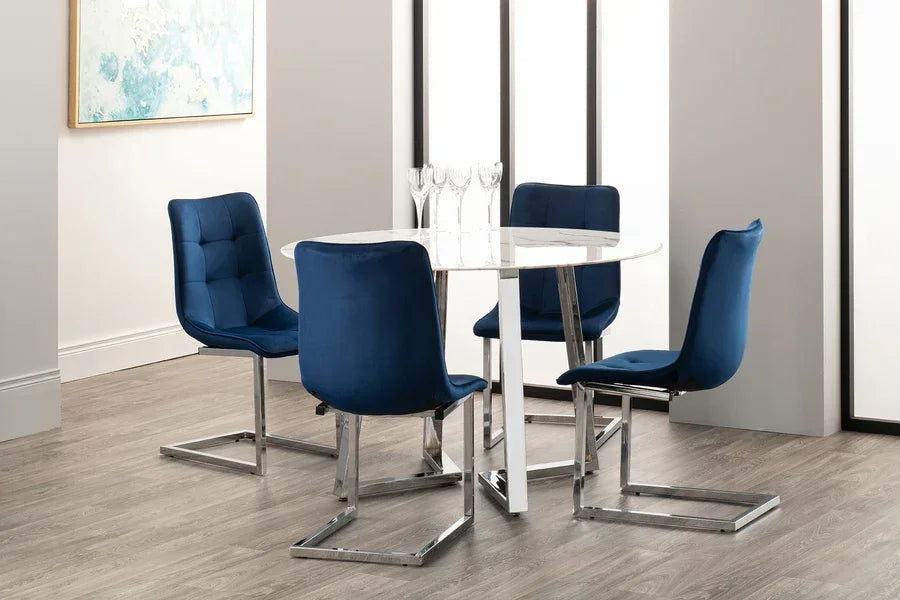 Round glass dining table with chrome legs and four blue velvet chairs in modern dining room