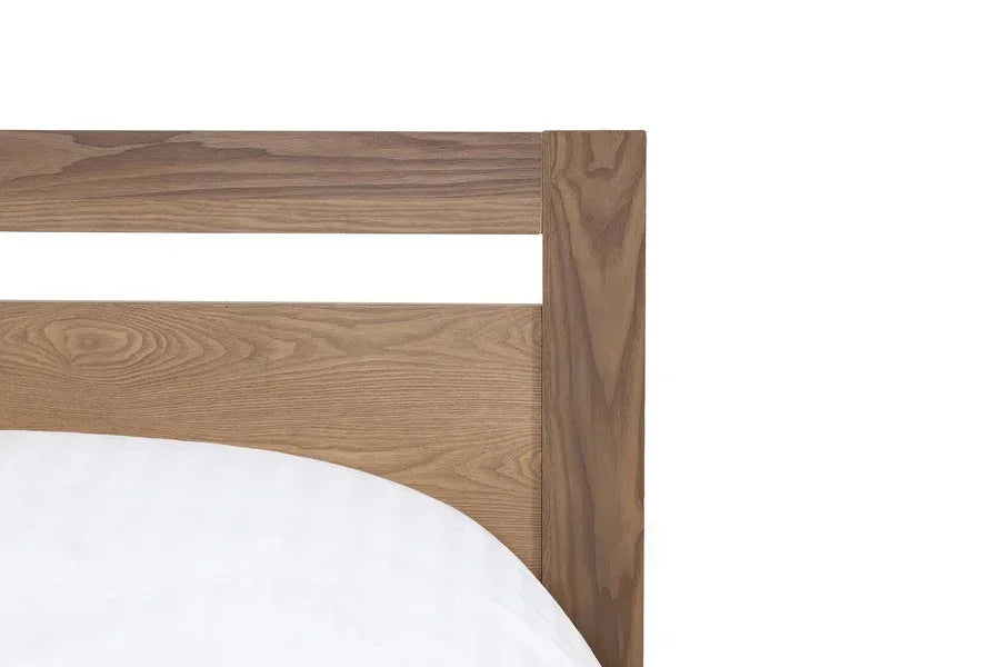 Oak wood bed frame corner with visible grain and white bedding
