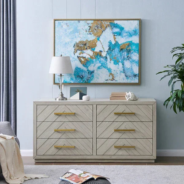 Light wood chest of drawers with gold handles in living room, artwork and lamp on top