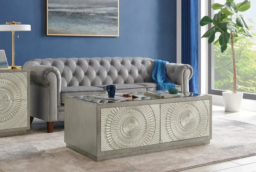 Grey velvet chesterfield sofa behind mirrored glass coffee table with radial pattern