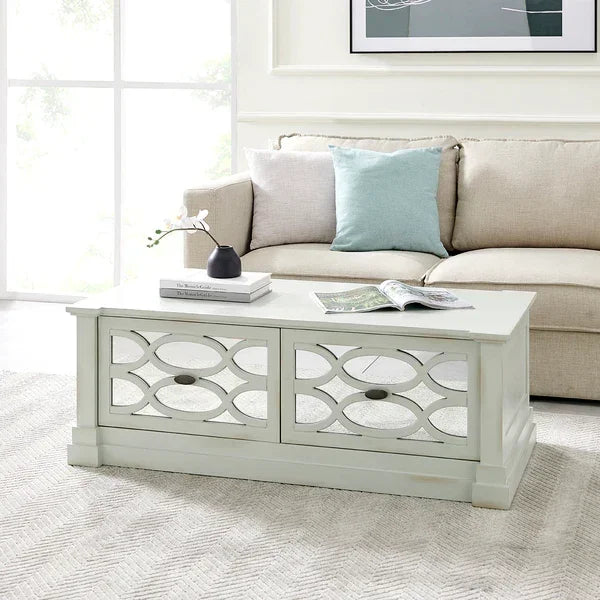 White wood coffee table with decorative glass panels in living room, sofa and cushions behind