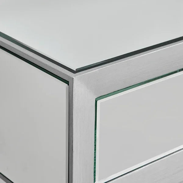 Close-up of mirrored bedside table corner with glass panel and silver trim