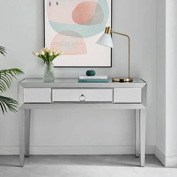Mirrored console table with drawer, gold desk lamp, books, and flowers in a glass vase
