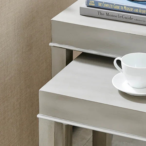 Light grey nesting tables with books and a white cup, shown in a living room corner