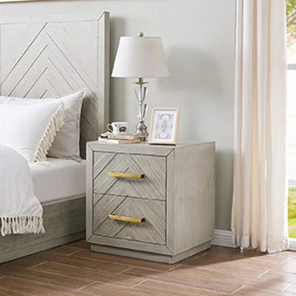 Light wood bedside table with gold handles and two drawers beside bed and lamp