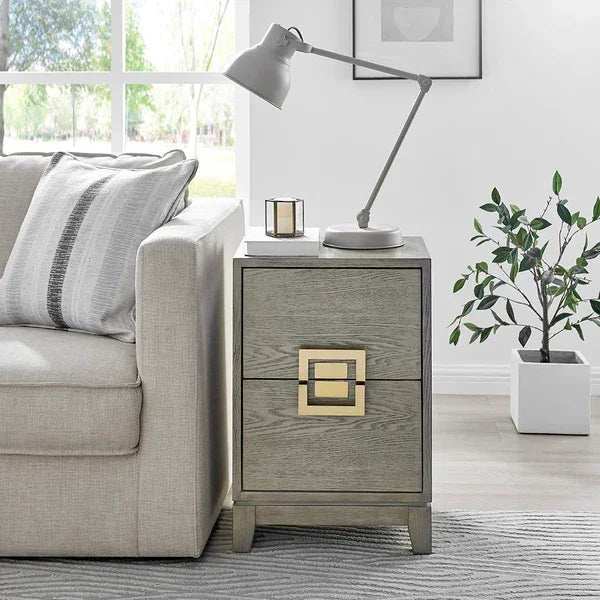 Grey wood bedside table with gold drawer handles beside sofa, lamp and plant nearby