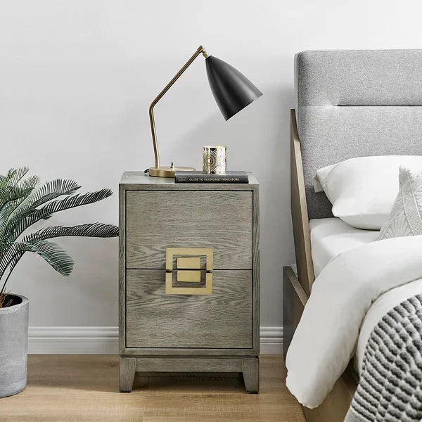 Grey wooden bedside table with gold handle beside upholstered bed, modern lamp on top