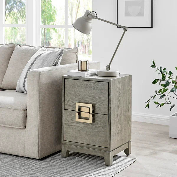 Grey wooden side table with two drawers and gold handles beside beige sofa in living room