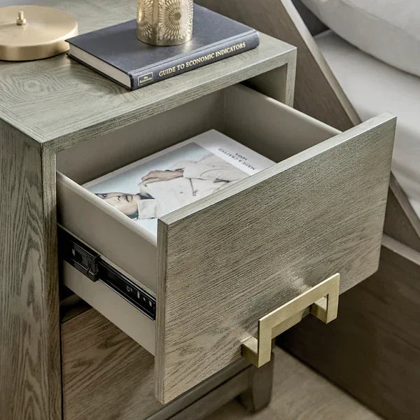 Wooden bedside table with drawer open, gold handle and book inside, next to bed