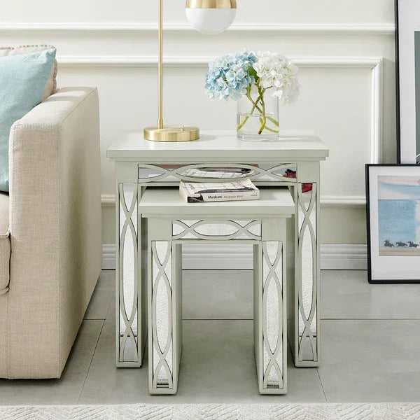 Mirrored nesting tables with decorative trim beside sofa, topped with lamp and vase