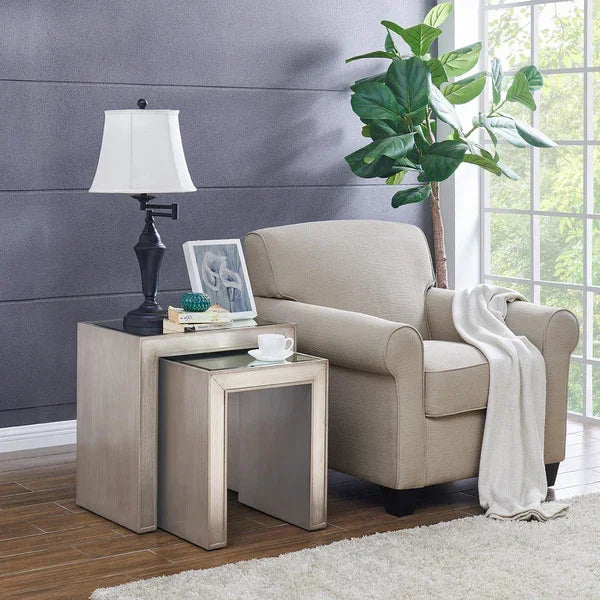 Beige armchair with nesting side tables, table lamp, and decorative plant by window