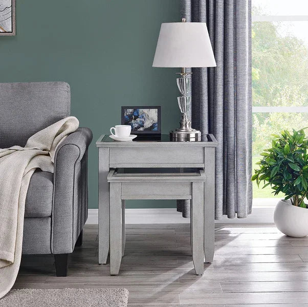 Light grey wooden nesting tables beside sofa with table lamp and decor accessories