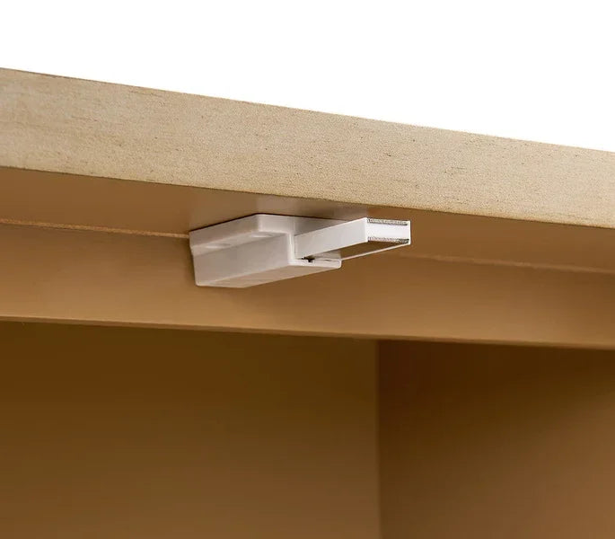 White drawer safety lock mounted underneath a wooden cabinet
