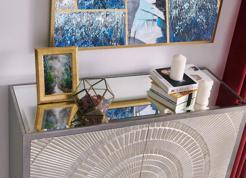 Mirrored sideboard with geometric doors, books, candles, and framed art decor on top