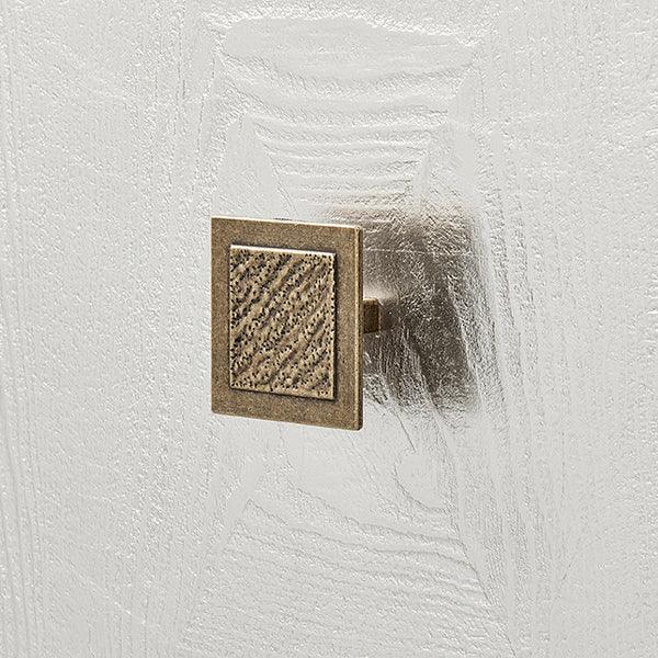 Square brass door knob with textured detail on white wooden cabinet