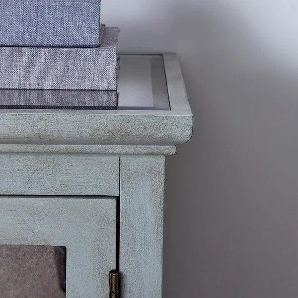Painted wooden bedside table with glass top and grey fabric books stacked on surface