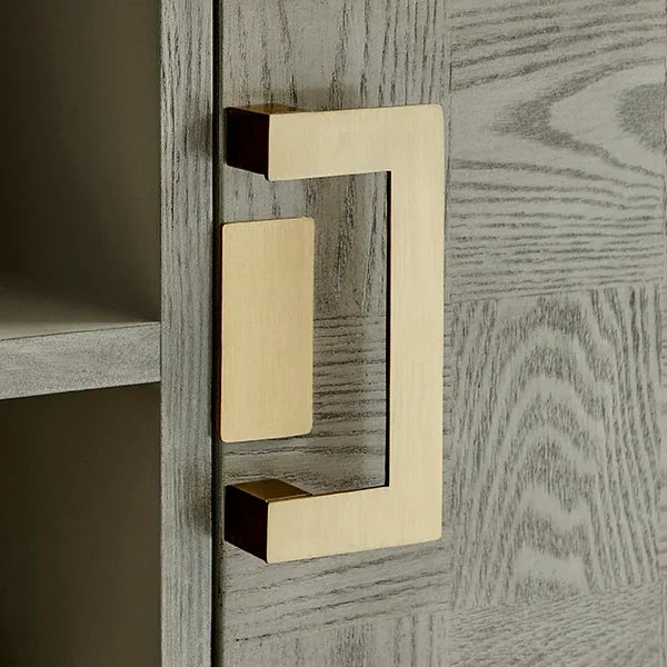 Gold metal cabinet handle on light wood grain furniture door, close-up view