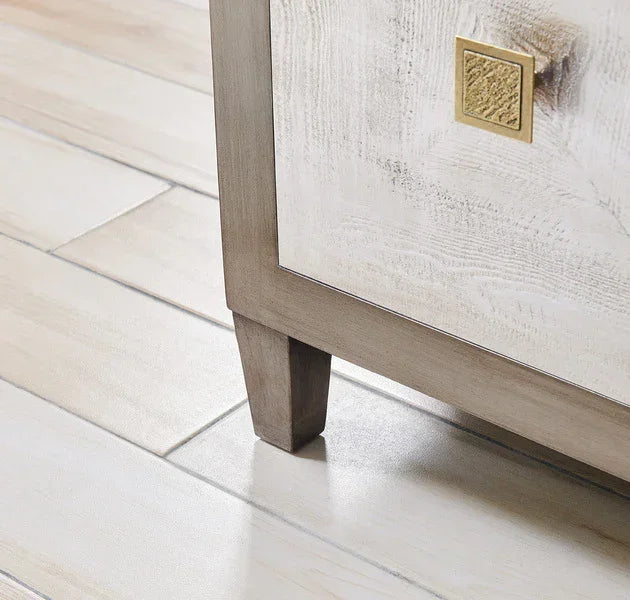 Closeup of wooden cabinet leg with textured gold handle on light tile floor