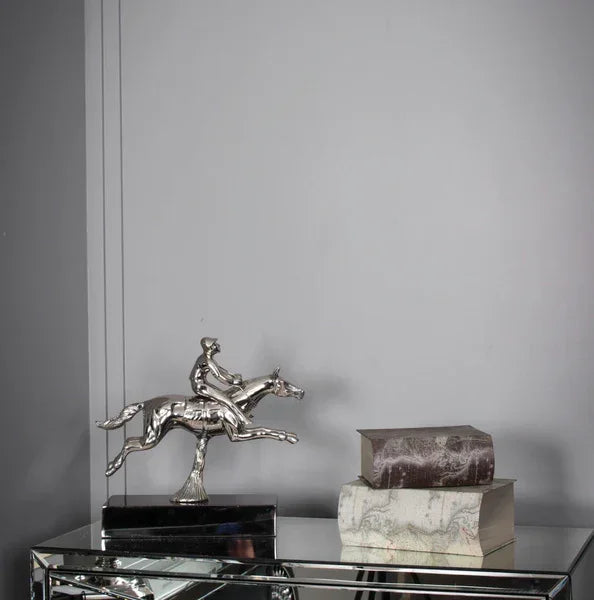 Silver horse and rider ornament next to stacked decorative books on mirrored console table