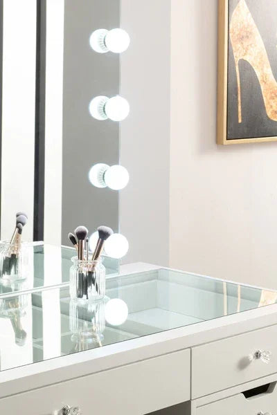 Glass top dressing table with mirror lights and makeup brushes in holder