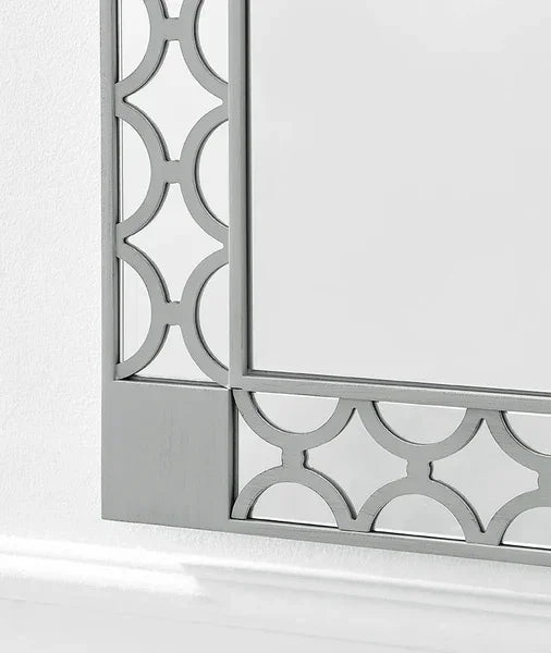 Silver geometric mirror frame with decorative cut-out pattern against a white wall