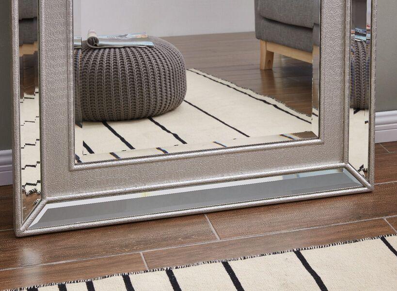 Silver framed mirror with textured border on wooden floor beside cream rug and pouffe