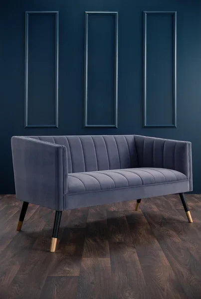 Grey velvet sofa with vertical channel tufting and gold-capped legs on dark wood floor
