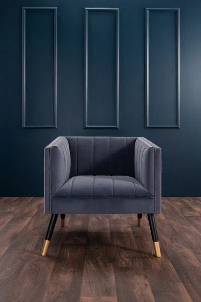 Dark blue velvet armchair with gold-tipped legs on wooden floor against navy wall