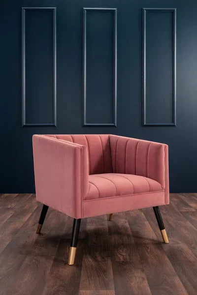 Blush pink velvet accent chair with gold-tipped legs on dark wooden flooring