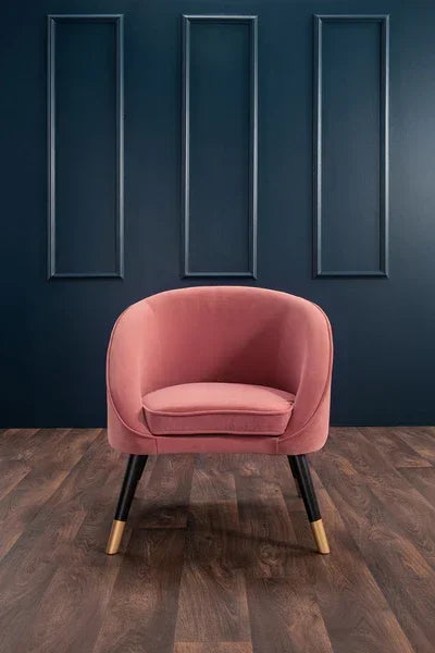 Pink velvet accent chair with black and gold legs on dark wood flooring